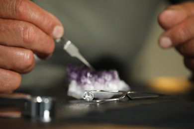 Photo of Professional jeweler working with beautiful amethyst at table, focus on tweezers