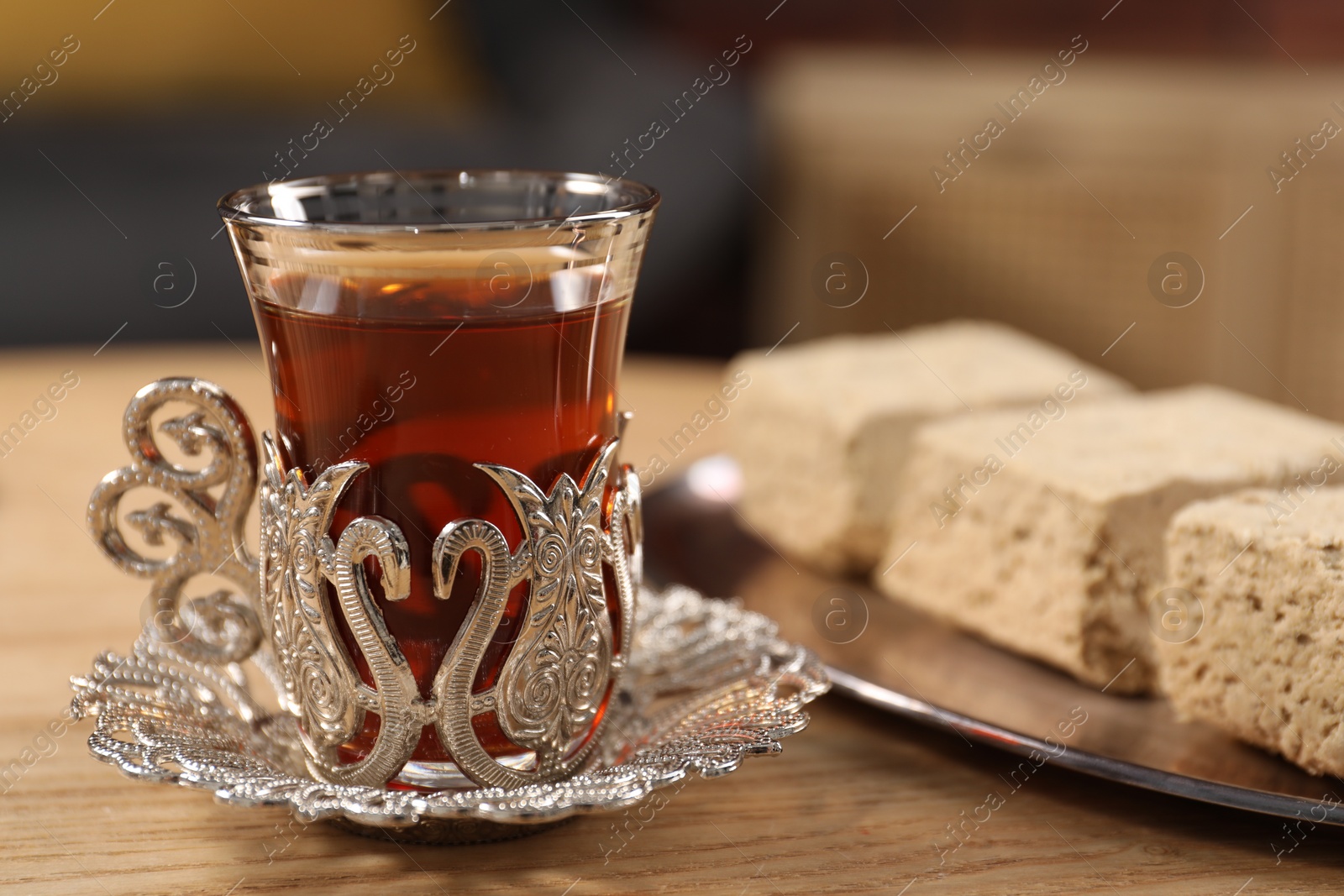 Photo of Glass of traditional Turkish tea in vintage holder and tasty halva on wooden table, closeup