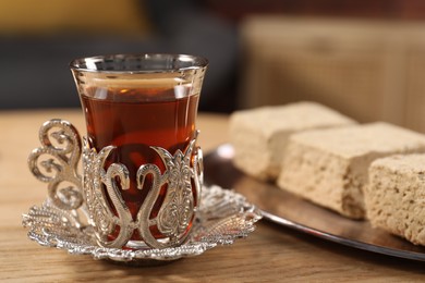 Glass of traditional Turkish tea in vintage holder and tasty halva on wooden table, closeup