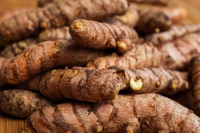 Many whole turmeric roots on wooden table, closeup
