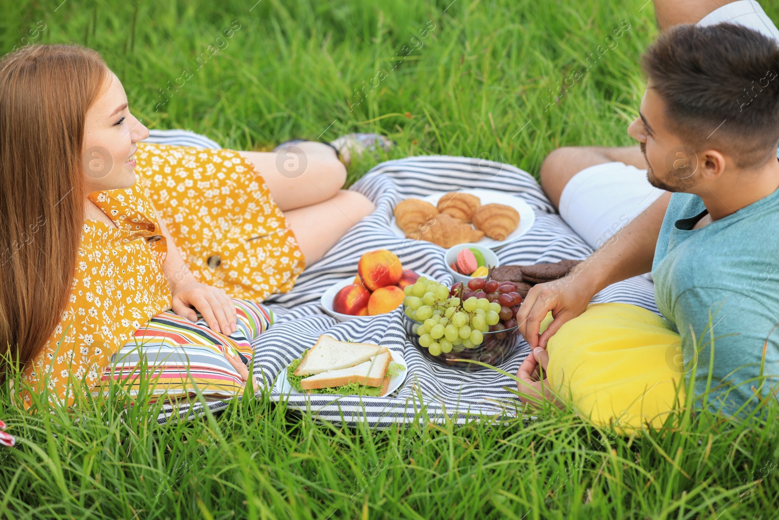 Photo of Happy young couple having picnic on green grass in park