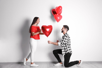 Photo of Happy young couple with heart shaped balloons near light wall. Valentine's day celebration