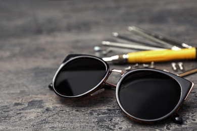 Stylish female sunglasses and fixing tools on grey table