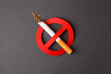 Photo of Cigarette with prohibition sign on dark grey background, top view. Quitting smoking concept