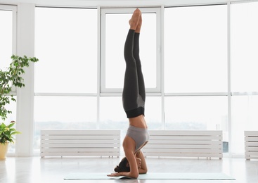 Photo of Young woman practicing supported headstand asana in yoga studio. Salamba Sirsasana pose