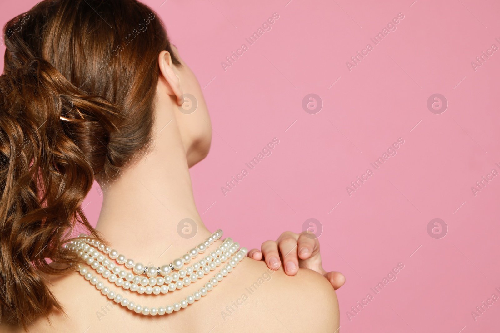 Photo of Young woman wearing elegant pearl necklace on pink background, back view. Space for text