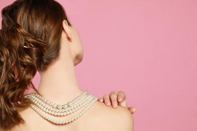 Photo of Young woman wearing elegant pearl necklace on pink background, back view. Space for text