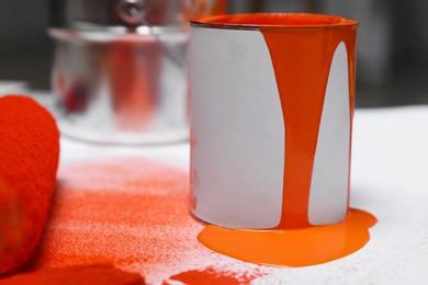 Photo of Can of orange paint and roller on white table indoors, closeup