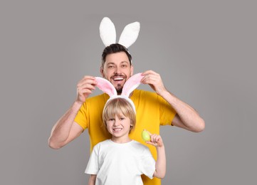 Photo of Father and son in bunny ears headbands having fun on grey background. Easter celebration