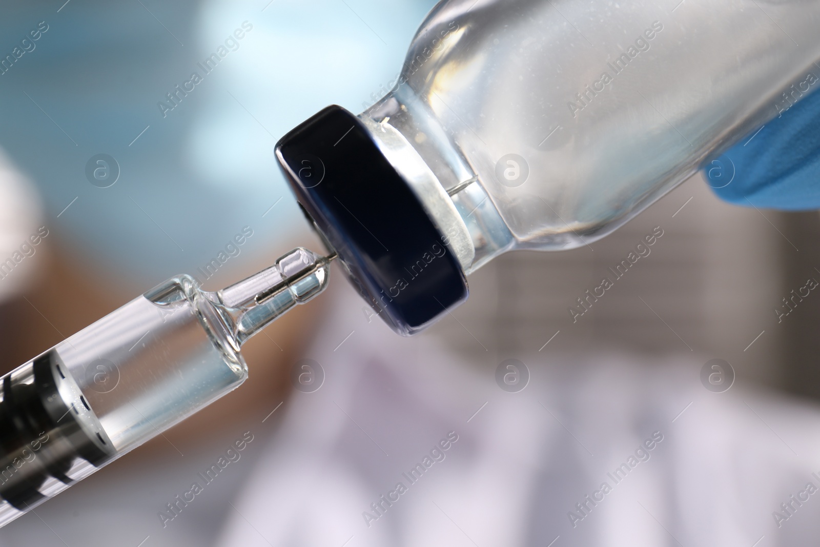 Photo of Woman filling syringe with vaccine from vial on blurred background, closeup