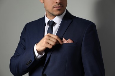 Man fixing handkerchief in breast pocket of his suit on light grey background, closeup