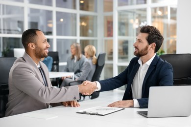 Photo of Lawyer shaking hands with client at table in office, selective focus