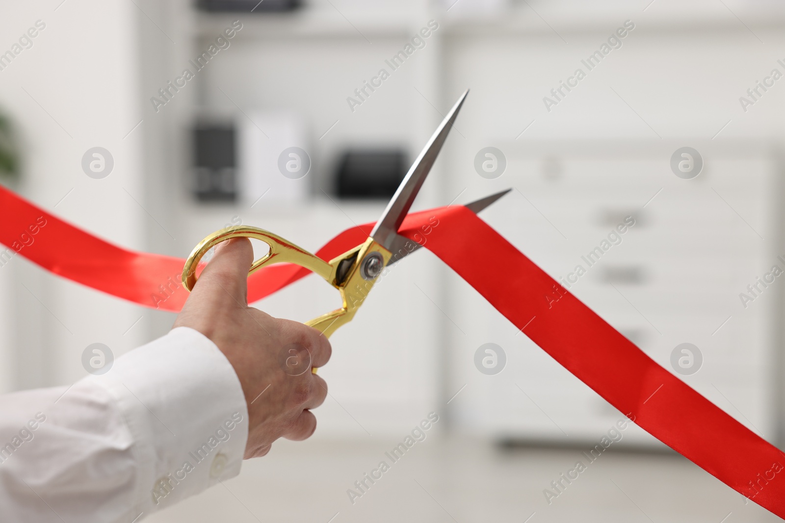 Photo of Woman cutting red ribbon with scissors indoors, closeup