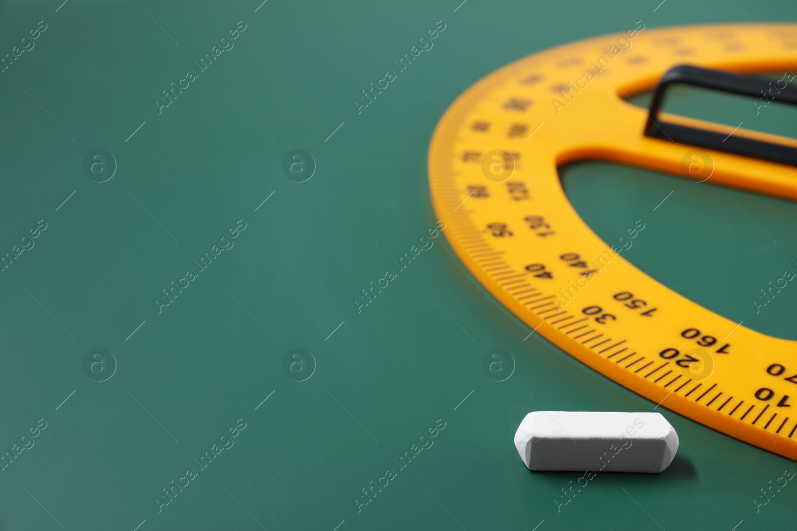 Photo of Yellow protractor and chalk on green chalkboard, closeup. Space for text