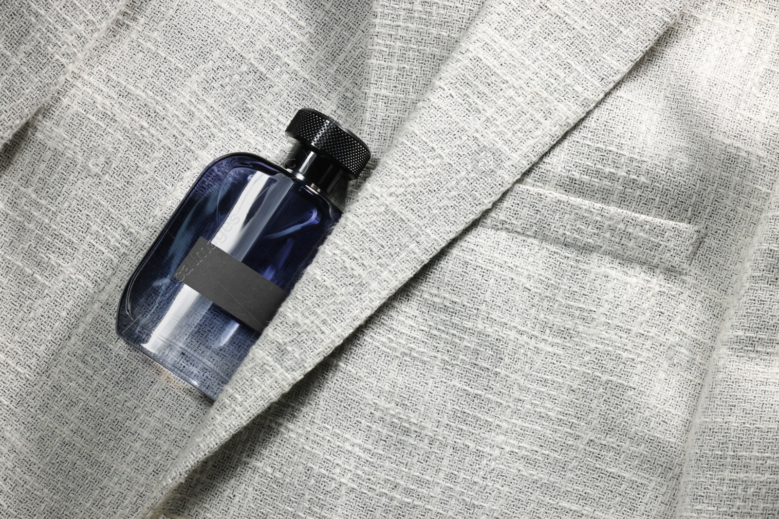 Photo of Luxury men's perfume in bottle on grey jacket, top view. Space for text