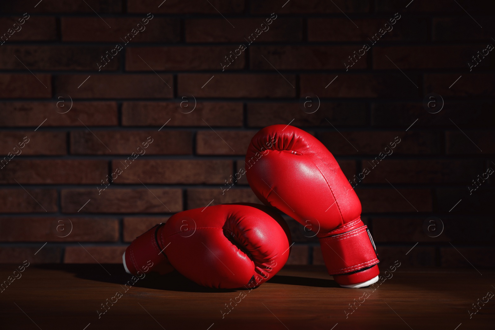 Photo of Pair of red boxing gloves on wooden table near brick wall