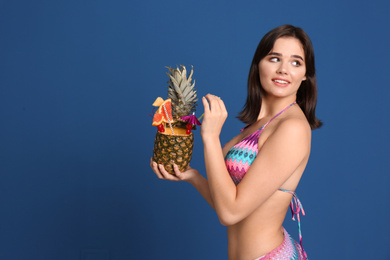Photo of Beautiful young woman with exotic cocktail wearing bikini on blue background. Space for text