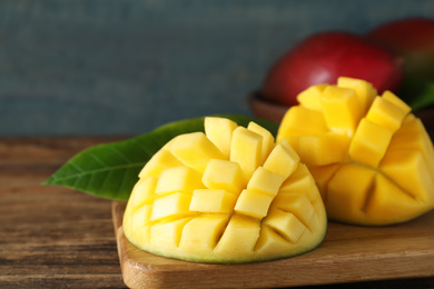 Photo of Halves of ripe mango cut into cubes on wooden table