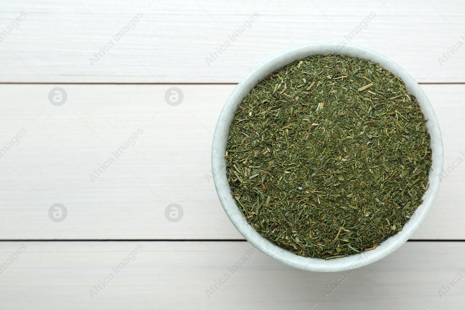 Photo of Dried dill in bowl on white wooden table, top view. Space for text
