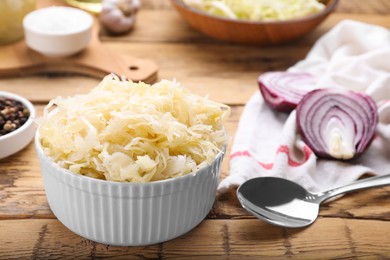 Photo of Bowl of tasty sauerkraut and ingredients on wooden table, closeup