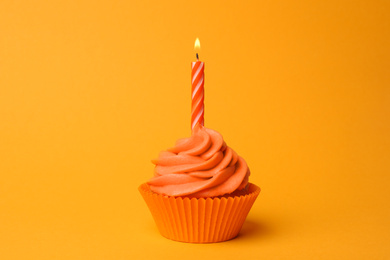 Photo of Delicious birthday cupcake with orange cream and burning candle on yellow background