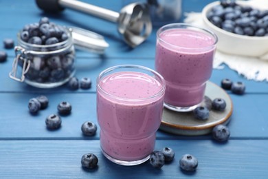 Photo of Glasses of blueberry smoothie with fresh berries on blue wooden table