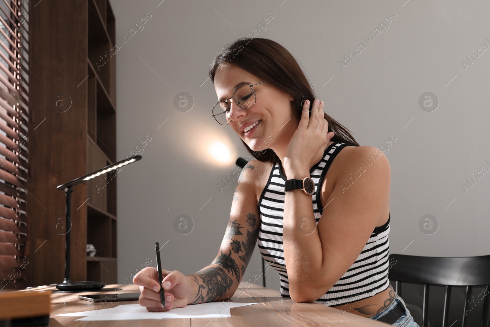 Photo of Beautiful woman with tattoos on body drawing in sketchbook at table indoors