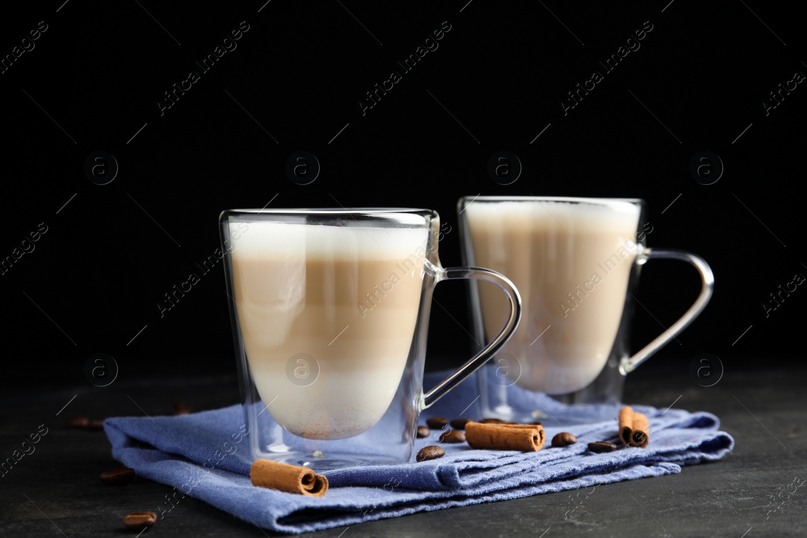 Photo of Delicious latte macchiato, cinnamon and coffee beans on grey table against black background