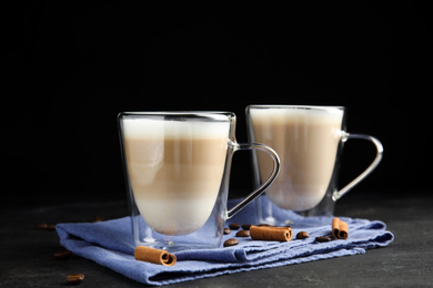 Photo of Delicious latte macchiato, cinnamon and coffee beans on grey table against black background