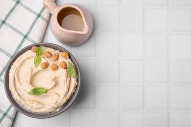 Photo of Delicious hummus with chickpeas served on white tiled table, flat lay. Space for text