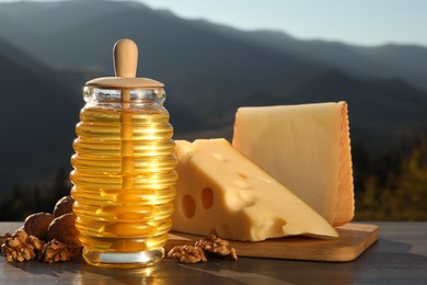 Photo of Fresh aromatic honey, cheese and nuts on wooden table against mountain landscape