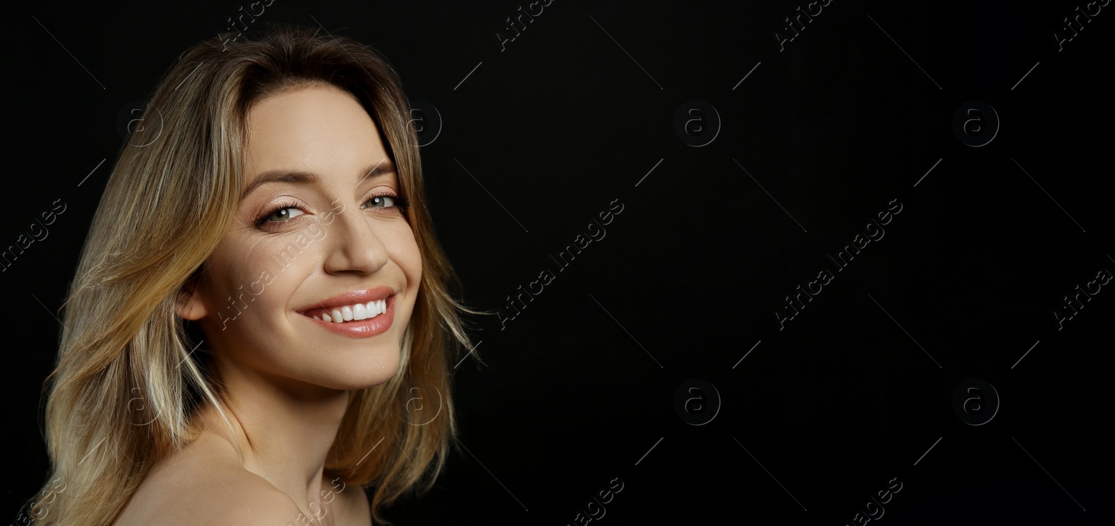 Photo of Portrait of happy young woman with beautiful blonde hair and charming smile on black background, closeup. Space for text