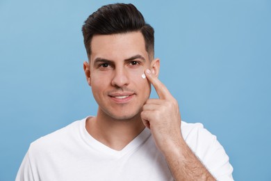 Happy handsome man applying face cream against turquoise background