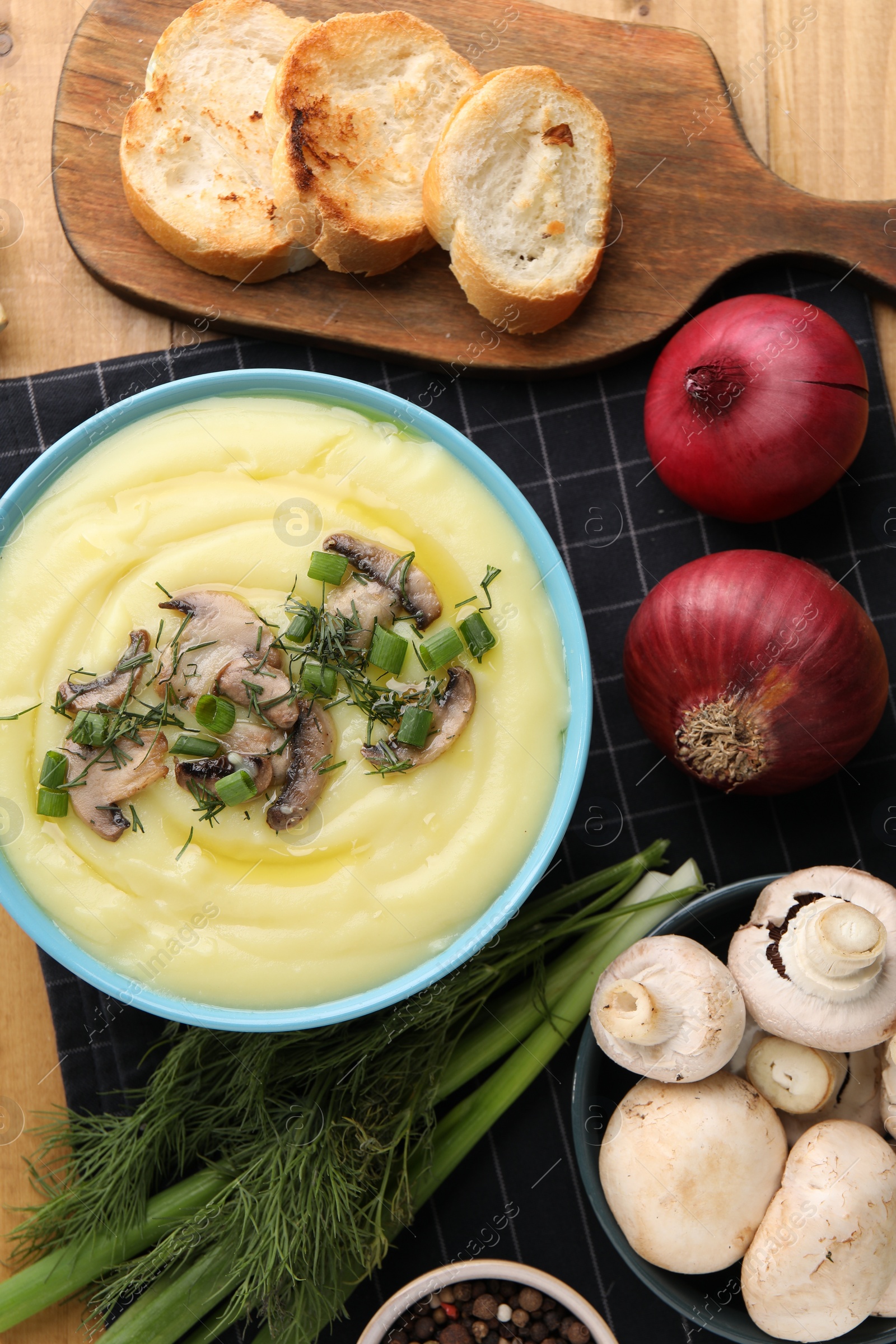 Photo of Bowl of tasty cream soup with mushrooms, green onions and dill on wooden table, flat lay