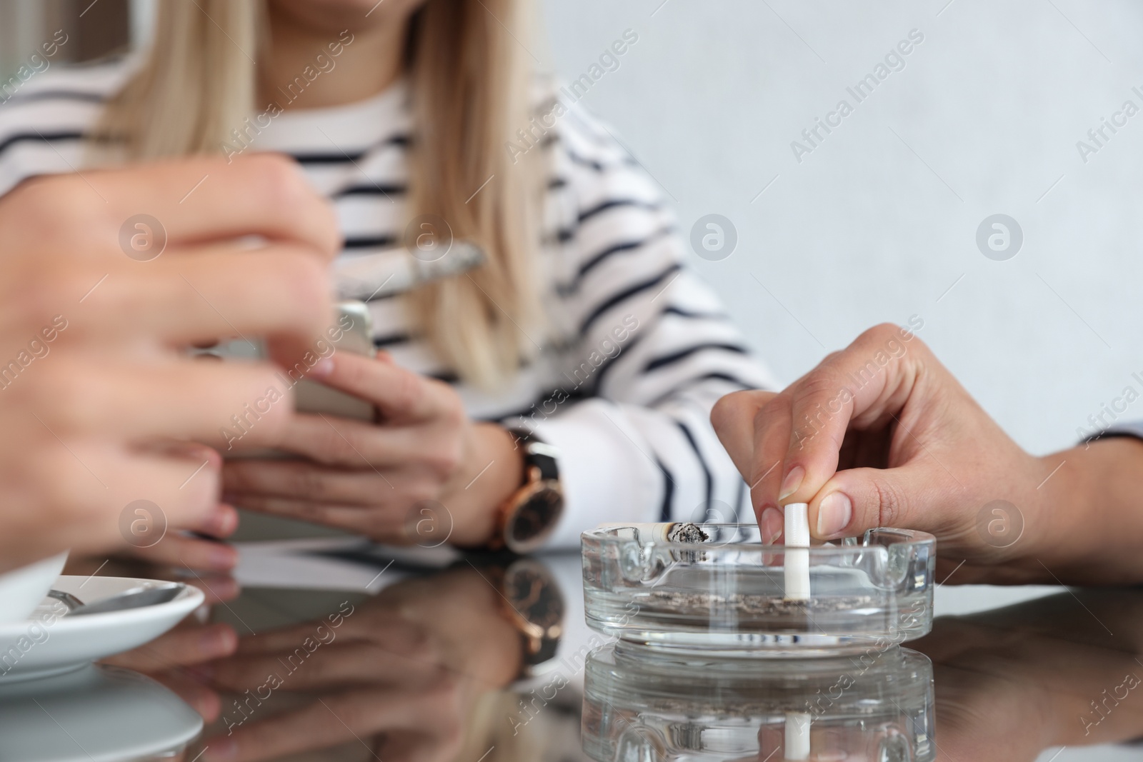 Photo of Woman putting out cigarette in ashtray at table, closeup