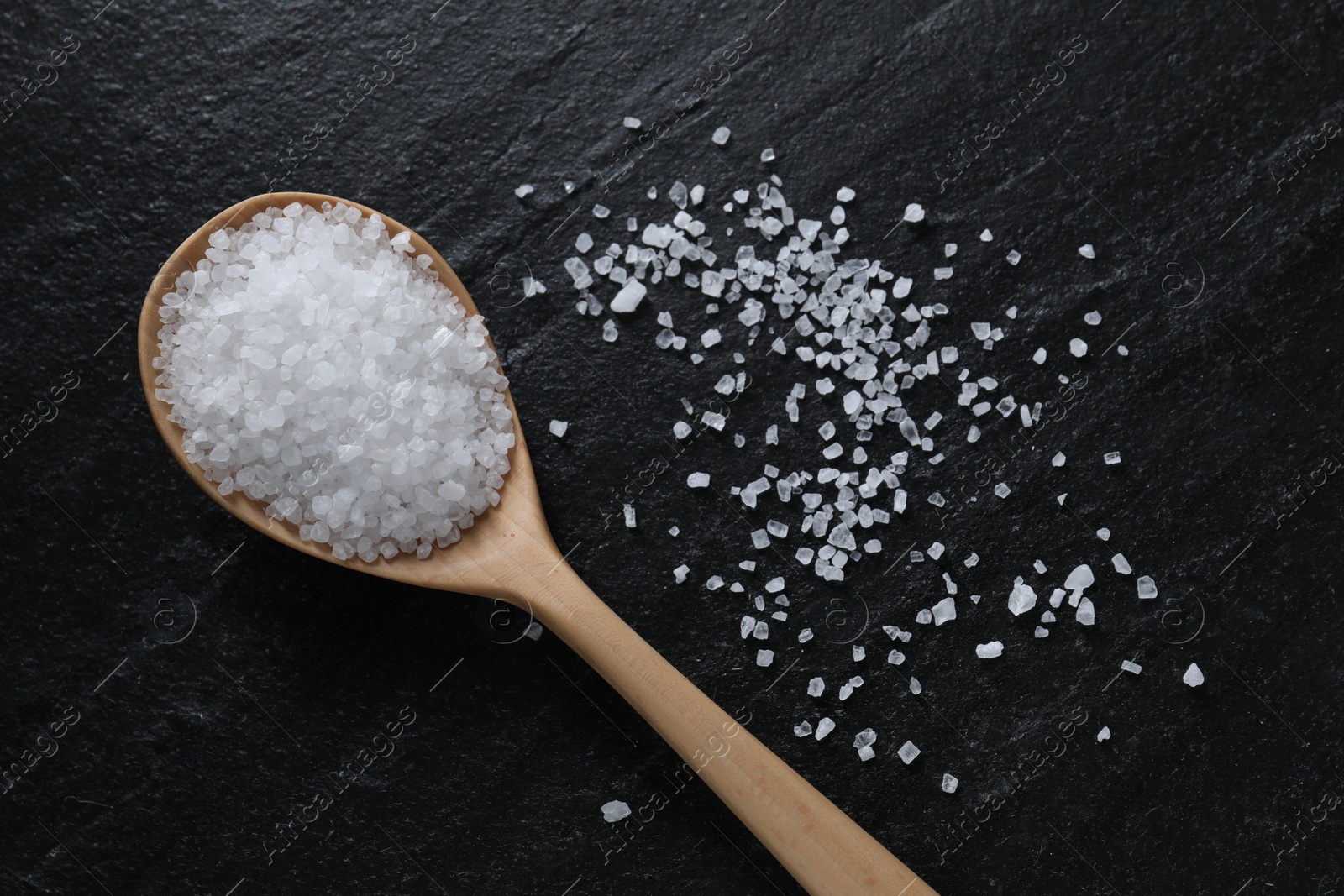 Photo of Organic white salt and spoon on black table, top view. Space for text