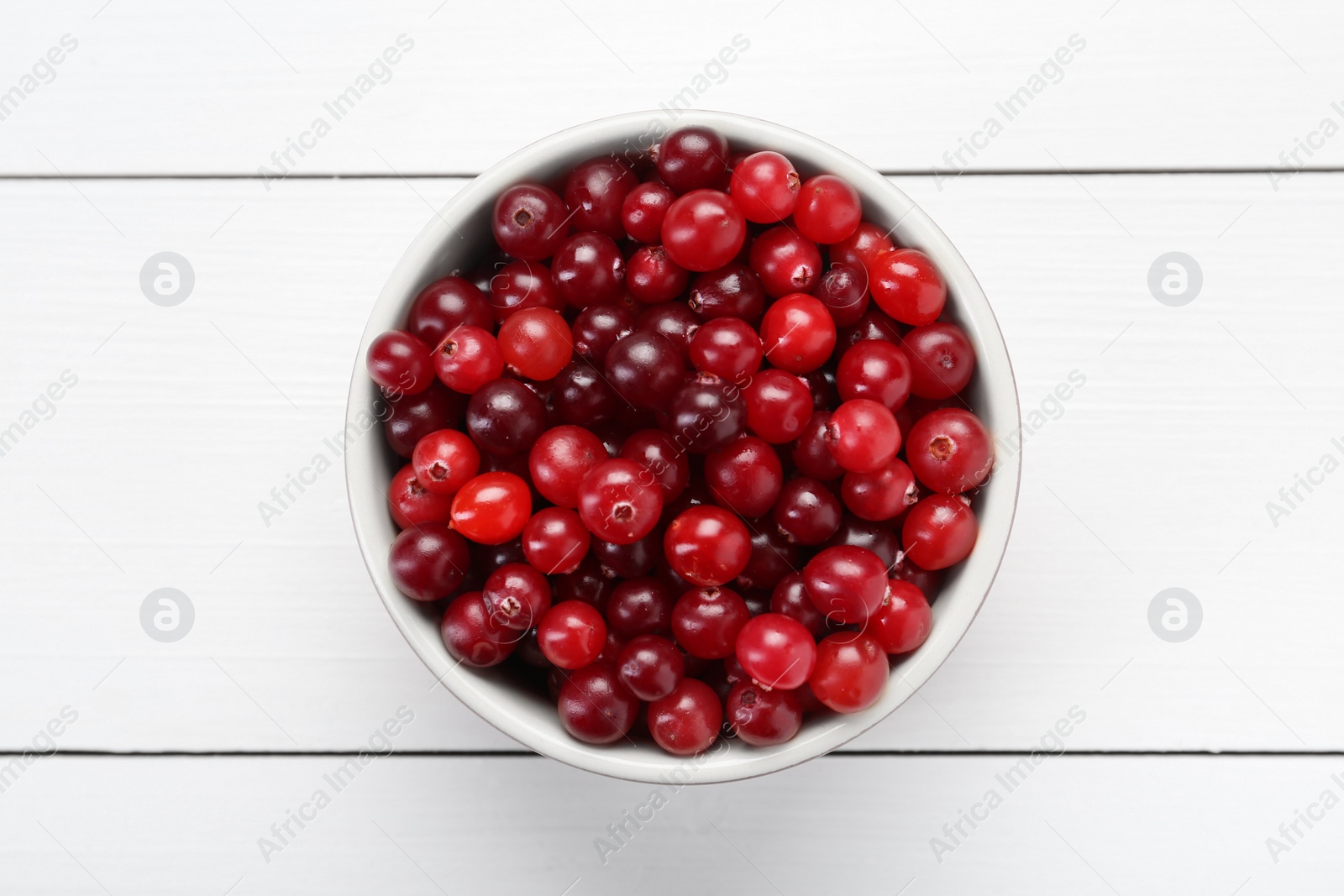 Photo of Fresh ripe cranberries in bowl on white wooden table, top view