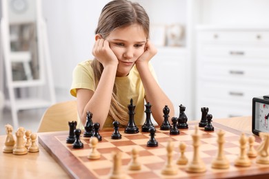 Cute girl playing chess at table in room