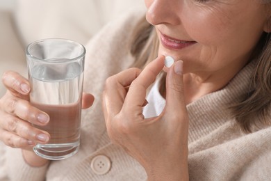 Photo of Senior woman with glass of water taking pill indoors, closeup