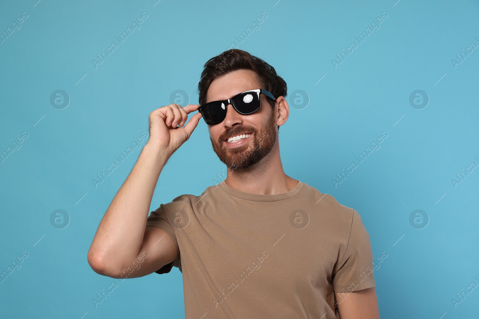 Photo of Portrait of smiling bearded man with stylish sunglasses on light blue background