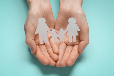 Photo of Woman holding paper family cutout on turquoise  background, closeup