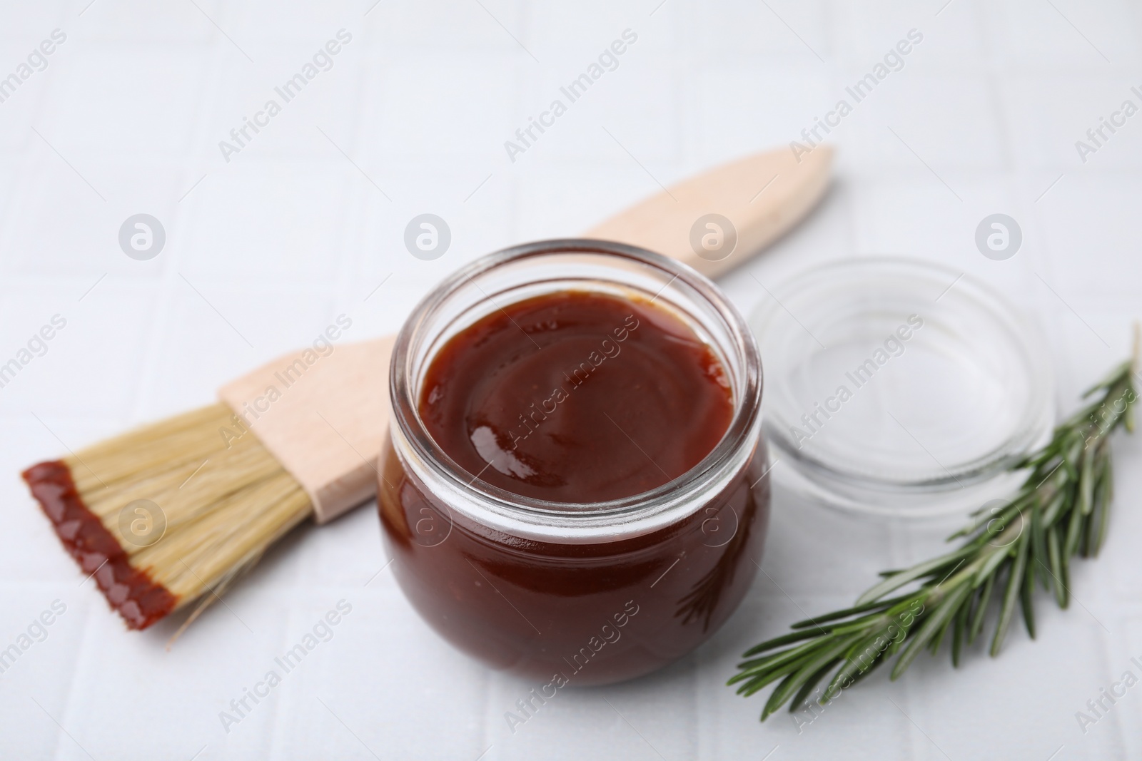 Photo of Marinade in jar, rosemary and basting brush on white tiled table