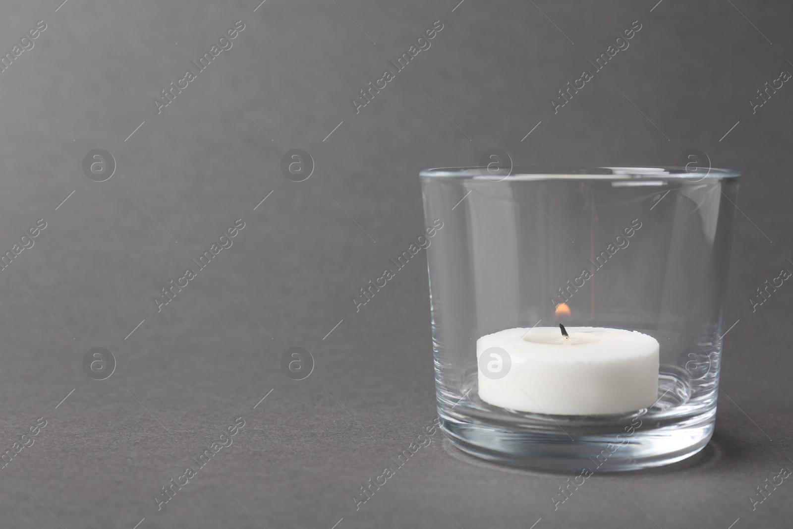 Photo of Candle in glass holder on grey background. Space for text