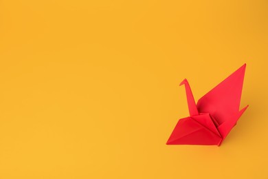 Photo of Origami art. Beautiful red paper crane on orange background, space for text