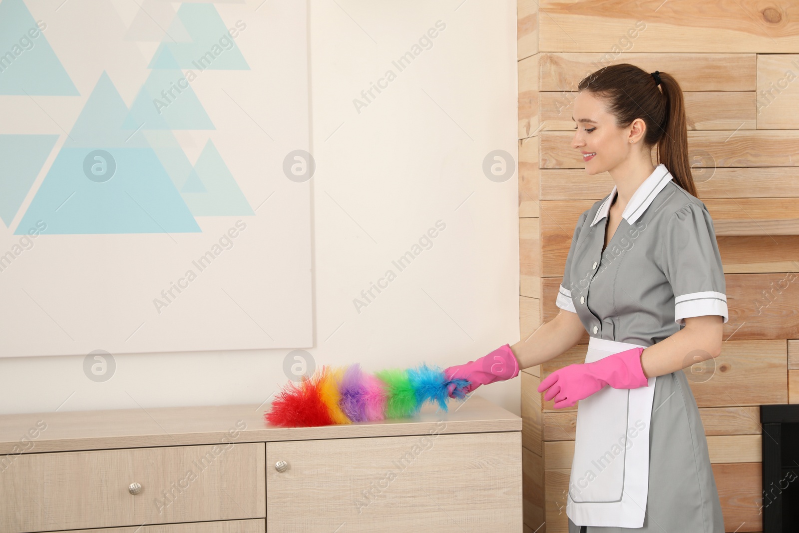 Photo of Young chambermaid wiping dust with brush in hotel room