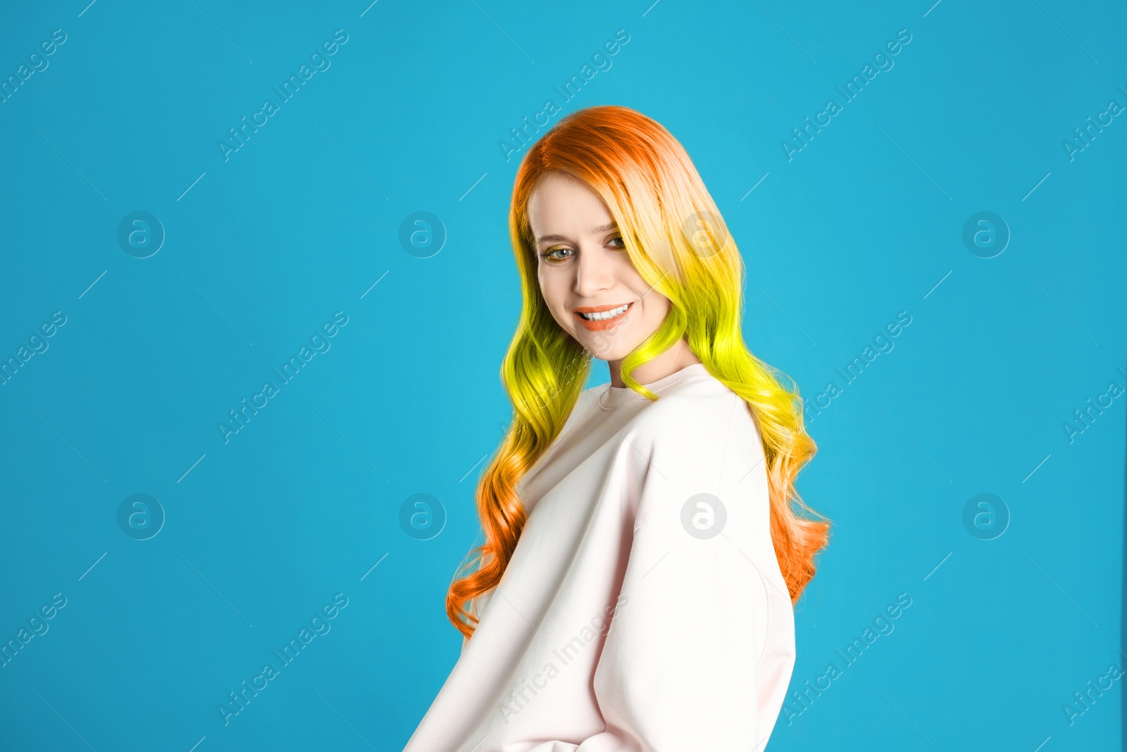 Image of Portrait of young woman with dyed long curly hair on blue background