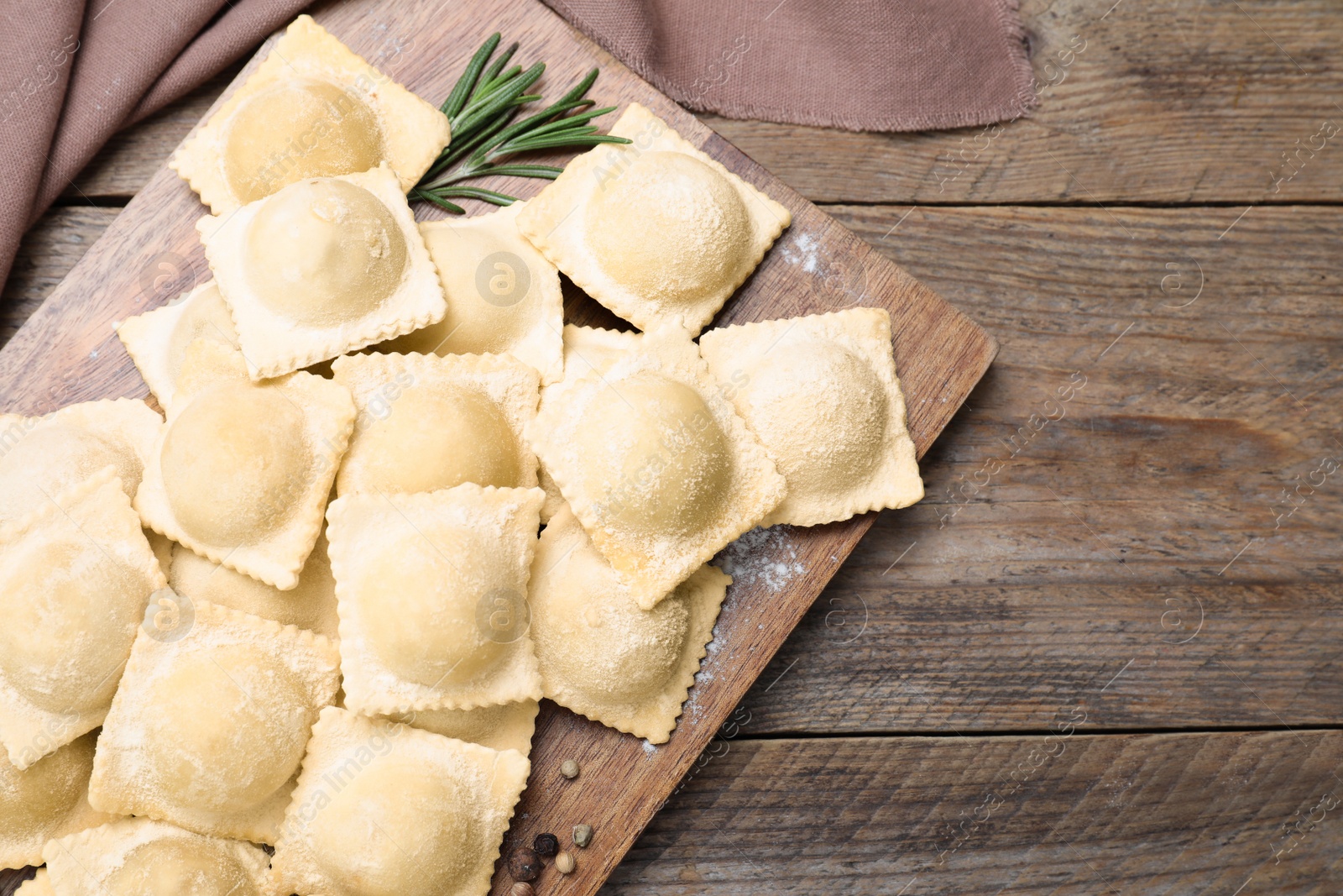 Photo of Uncooked ravioli and rosemary on wooden table, flat lay. Space for text