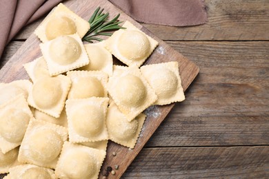 Photo of Uncooked ravioli and rosemary on wooden table, flat lay. Space for text