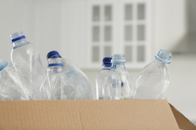 Photo of Cardboard box with used plastic bottles indoors, closeup. Recycling problem