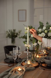 Photo of Woman lightning up candle at dining table indoors, closeup. Festive setting